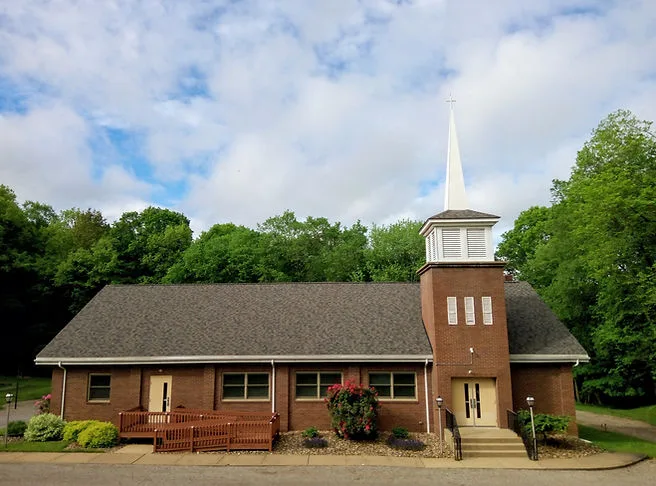 Cannelton Baptist Church, a brick building with a white steeple, surrounded by green trees in summer